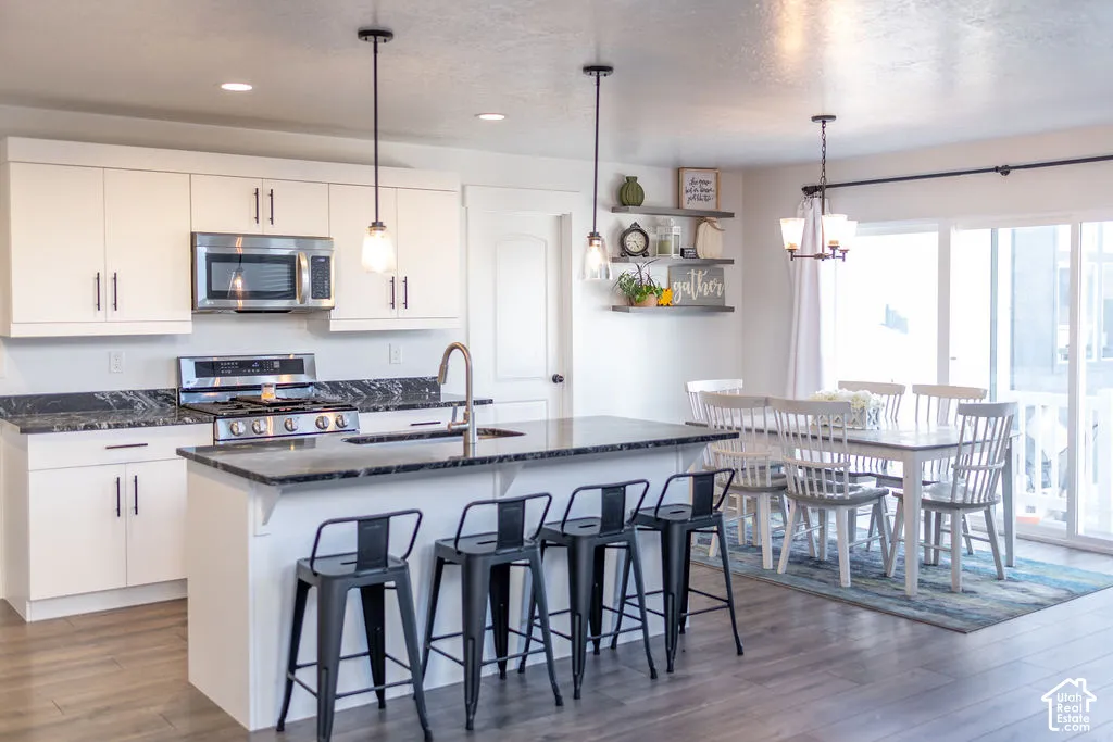 Kitchen with white cabinetry, dark stone-finish countertops, stainless steel appliances, a center island with sink, and wood-finish flooring