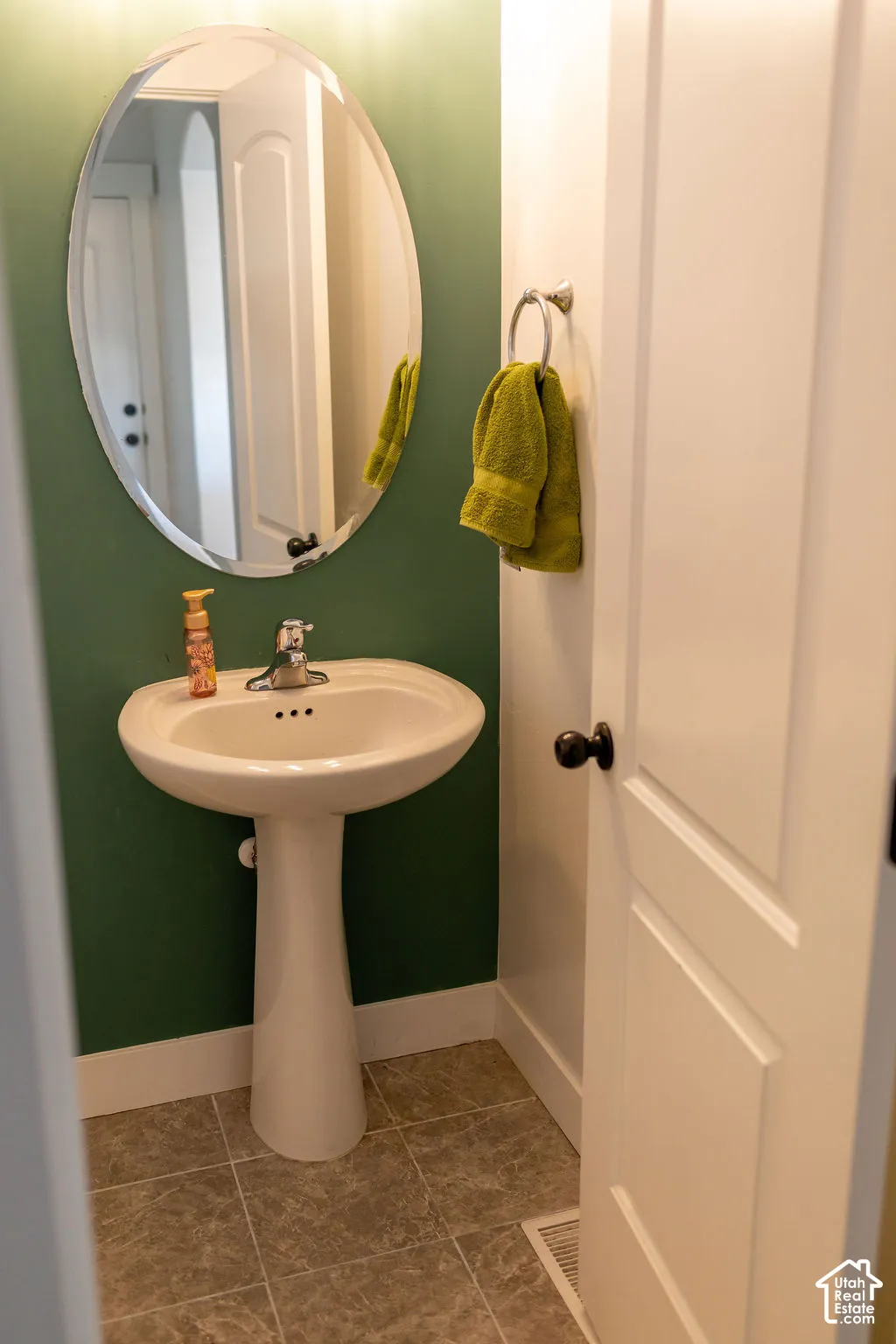 Pedestal sink with chrome faucet, oval mirror, and durable tile flooring