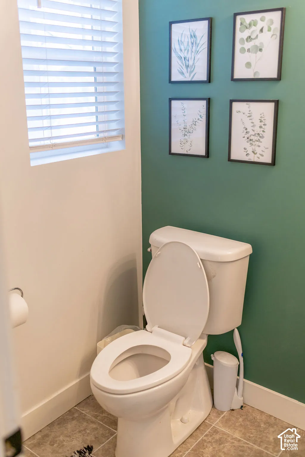 White toilet with a neutral-toned tile floor and a window featuring horizontal blinds