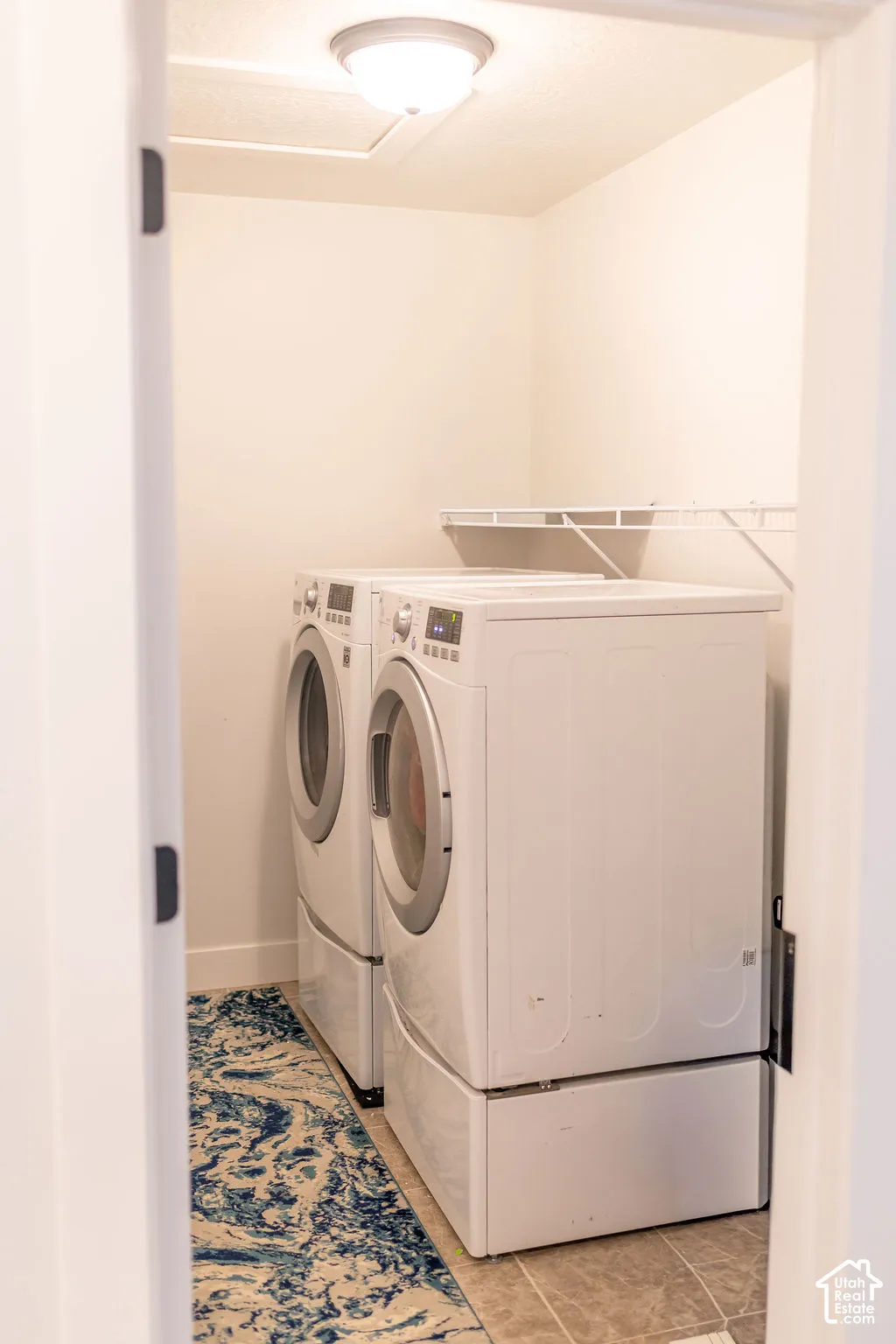 Laundry room featuring light-toned tile flooring, built-in wire shelving, and a flush mount ceiling light