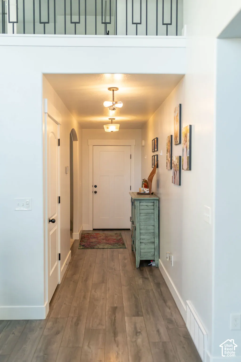 Hallway featuring wood-finish flooring, recessed lighting, white trim, and a contemporary black metal railing