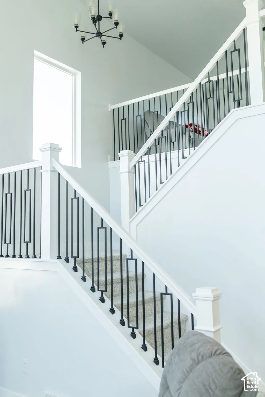 Split-level staircase featuring carpeted treads, white newel posts, and decorative black metal balusters