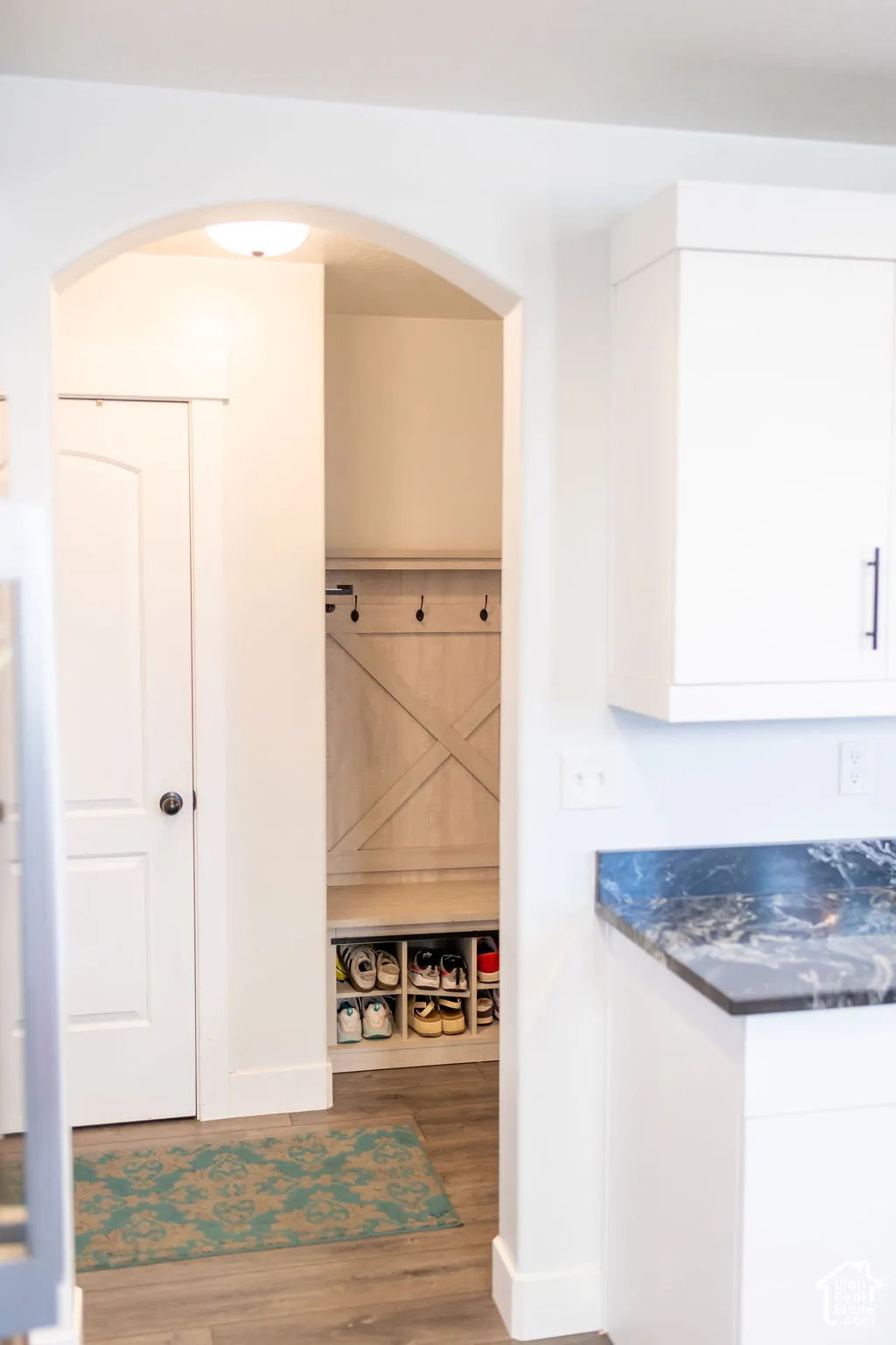 Archway entry to a built-in mudroom bench with cubby storage, featuring wood-finish flooring and a dark stone-finish countertop