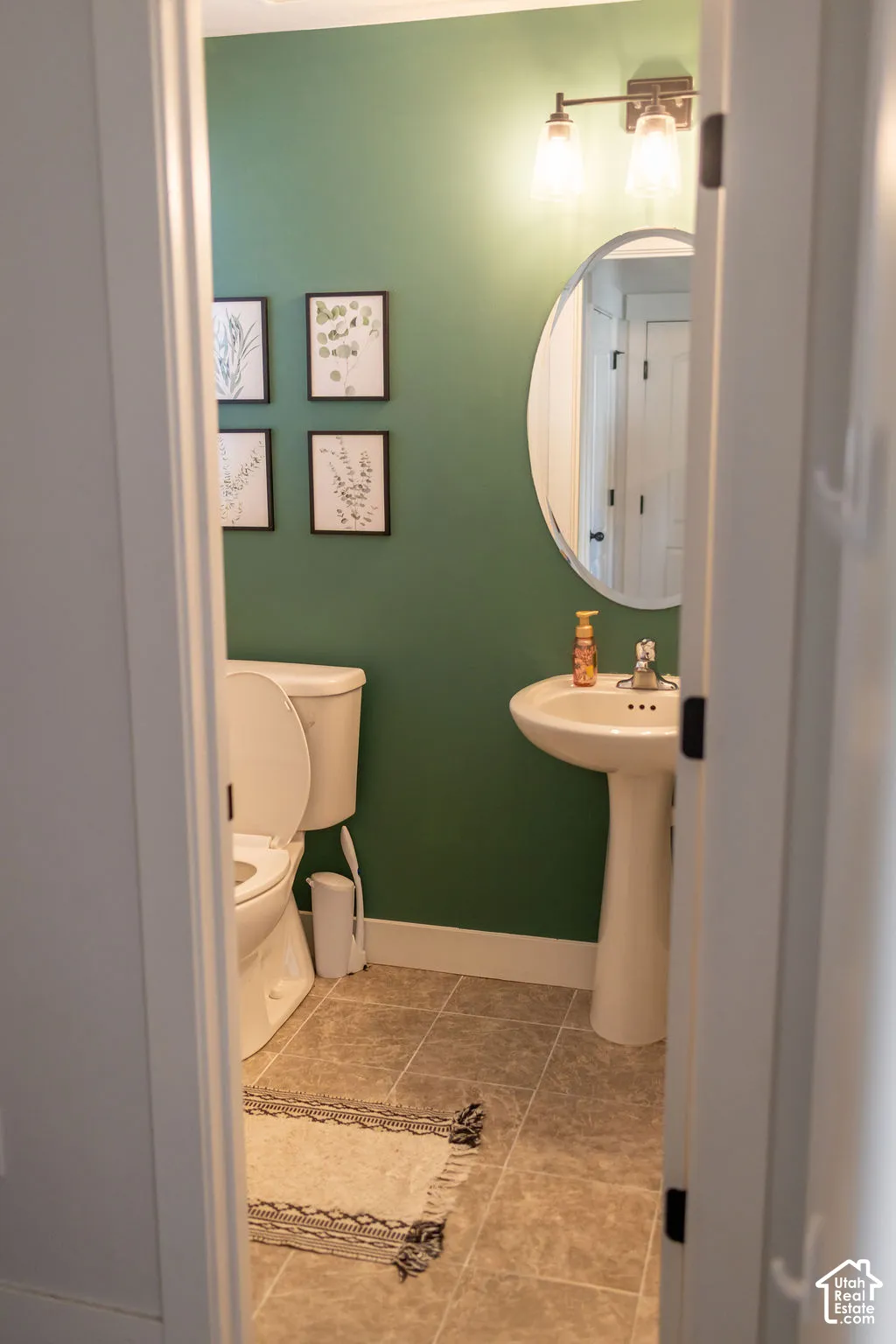 Pedestal sink with chrome faucet, wall-mounted light fixture, and tiled flooring