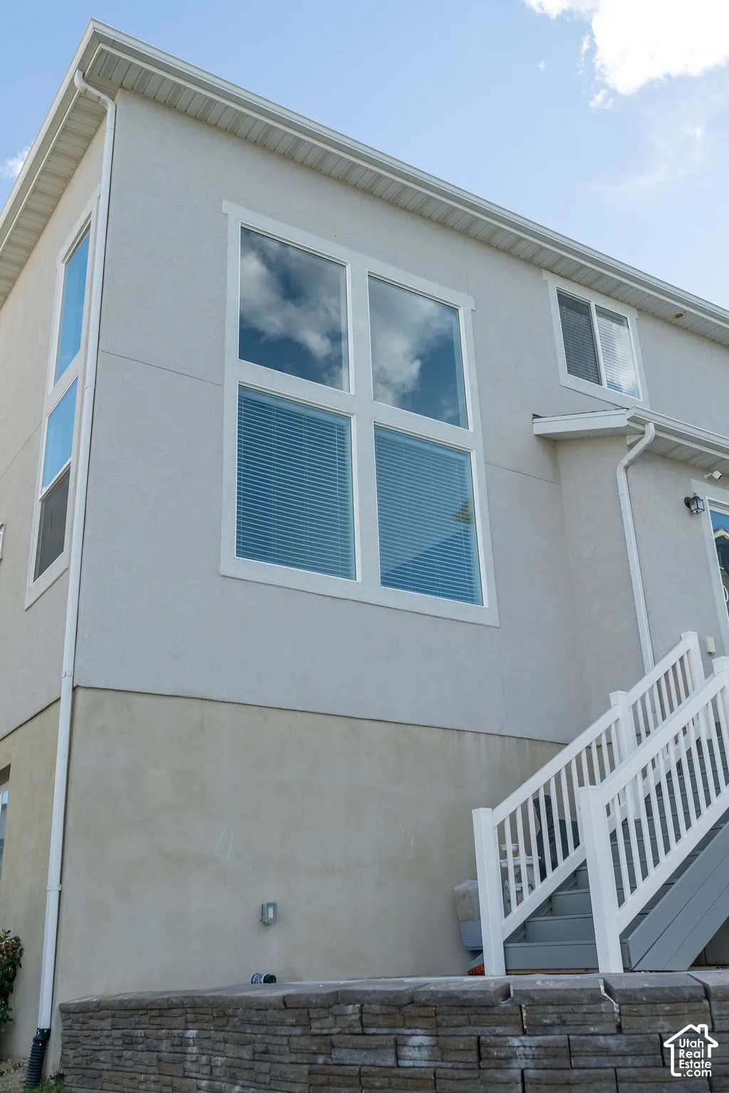 Stucco exterior with multiple window styles, including a large multi-pane window with white trim, and a white-railed exterior staircase with gray treads