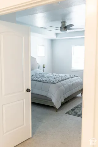 Carpeted room with a contemporary ceiling fan, tray ceiling, and dual windows with blinds
