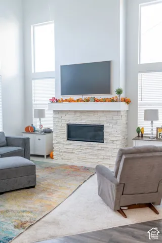 Two-story living area with high ceilings, multiple large windows, a stone-finish fireplace, and a built-in television
