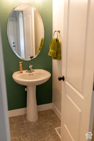Pedestal sink with chrome faucet, oval mirror, and durable tile flooring