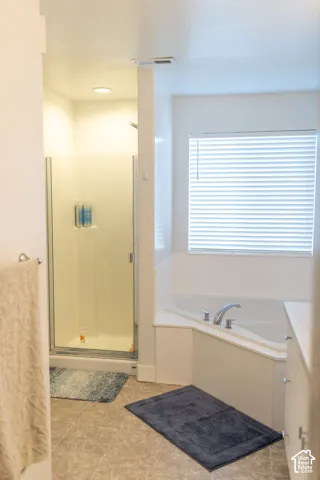 Corner soaking tub with chrome fixtures, glass-enclosed shower, tiled flooring, and a window with blinds