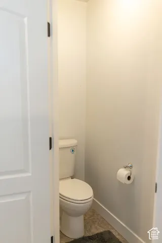 White two-panel door with dark hardware, a white toilet, chrome toilet paper holder, and tile flooring