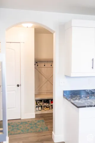 Archway entry to a built-in mudroom bench with cubby storage, featuring wood-finish flooring and a dark stone-finish countertop