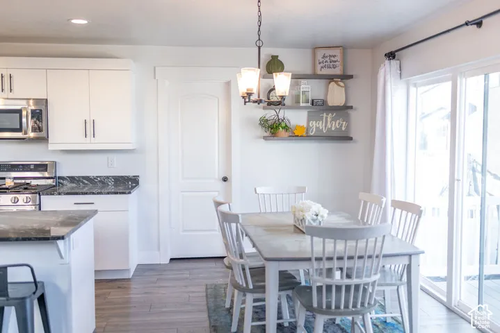 Kitchen and dining area featuring white cabinetry, dark countertops, wood-finish flooring, a stainless steel microwave, and sliding glass doors