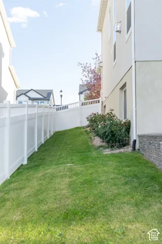 Expansive side yard featuring a manicured lawn, white privacy fencing, mature shrubbery, and stone veneer foundation detailing