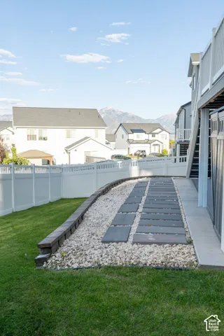 Expansive backyard featuring a green lawn, white privacy fence, and a stone retaining wall