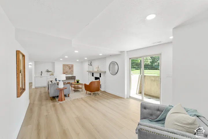 Wood-finish flooring throughout, white painted brick fireplace with mantel, recessed lighting, built-in wet bar with cabinetry, and sliding glass door