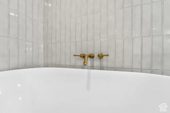 White bathtub with light gray vertical subway tile surround and wall-mounted brass fixtures