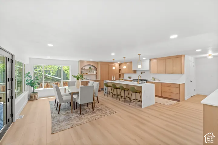 Light wood-finish flooring throughout, kitchen with light wood cabinetry, white countertops, and a white tile backsplash