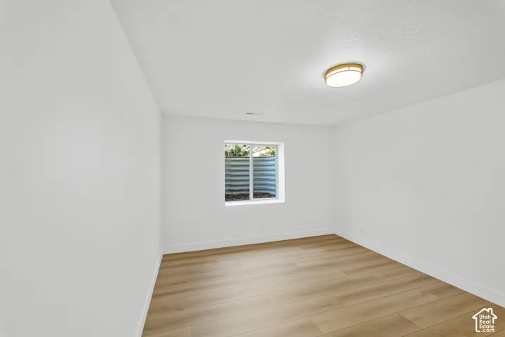 Recessed window with corrugated metal window well, wood-finish flooring, white walls, and flush-mount ceiling light