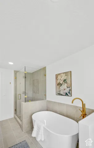 Freestanding soaking tub with a floor-mounted gold-tone faucet, glass-enclosed shower, and coordinating tile flooring and wainscoting
