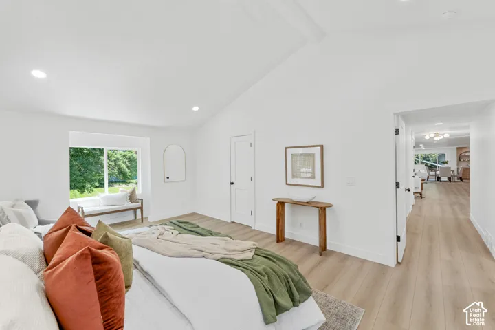 Vaulted ceiling with recessed lighting, light wood-finish flooring, white walls, and a large window with a built-in bench