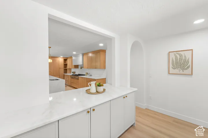 Built-in cabinetry with a white countertop and gold-finish hardware, archway detail, recessed lighting, and wood-finish flooring