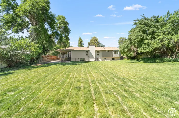Expansive backyard featuring a manicured lawn, mature trees, and a raised wooden deck