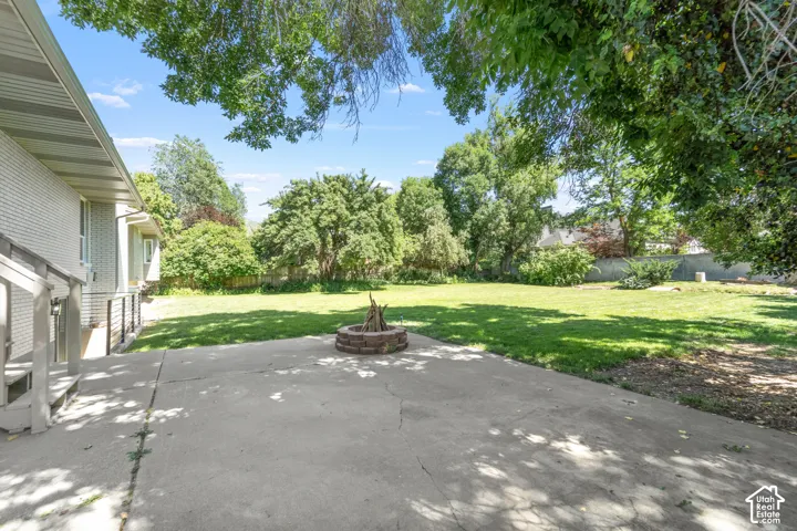 Expansive backyard featuring a brick fire pit, concrete patio, and mature trees