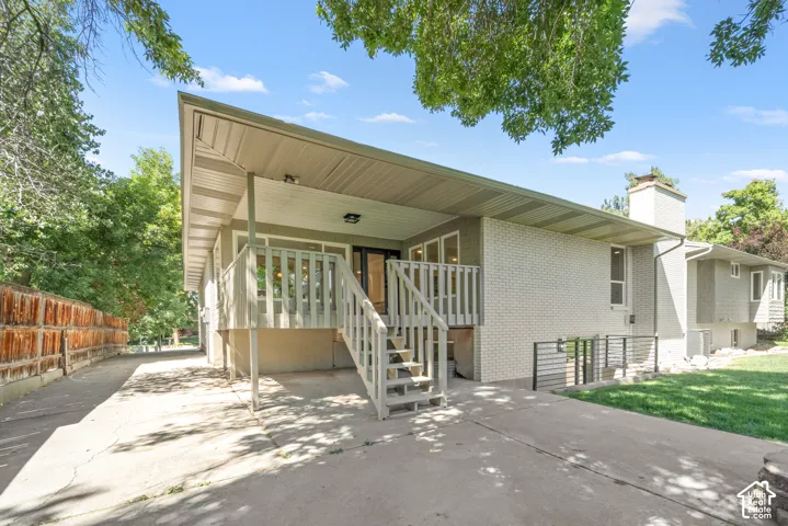 Covered outdoor patio with a staircase leading to a concrete patio, brick exterior, and a manicured lawn