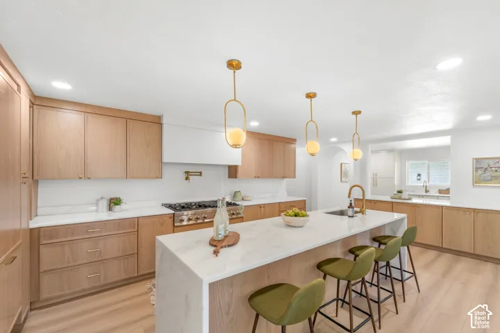 Kitchen featuring a central island with an undermount sink, brass-finish fixtures, light wood-finish cabinetry, and recessed lighting