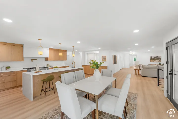 Open-concept living area with wood-finish flooring, a kitchen featuring wood cabinetry and an island with a waterfall countertop, recessed lighting, and a dining area