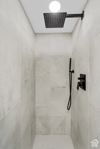 Tiled shower enclosure featuring a matte black rainfall showerhead, handheld shower, and control valve