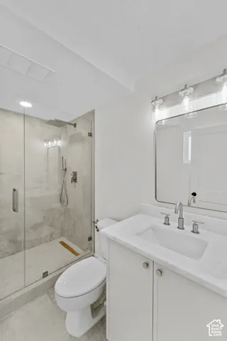 Frameless glass shower enclosure with rainfall showerhead, white vanity with integrated sink, polished chrome fixtures, and overhead vanity lighting