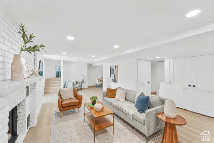 Recessed lighting illuminating wood-finish flooring, a painted brick fireplace, built-in storage closets, and a built-in stairwell
