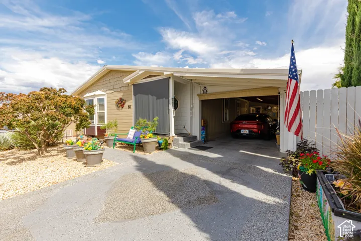 Carport with paved driveway, white picket fence, and established landscaping