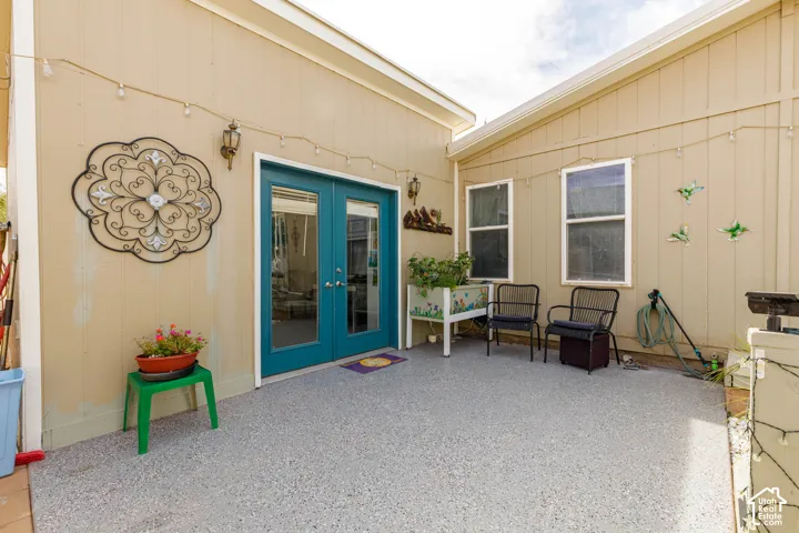 Covered patio with concrete flooring, teal French doors with glass panels, decorative metal wall art, and multiple windows providing natural light