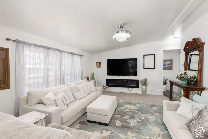 Vaulted ceiling with a chandelier, wall-mounted electric fireplace, and a large window with horizontal blinds