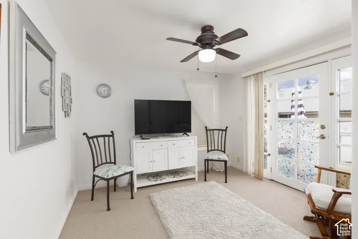 Ceiling fan with integrated lighting, glass-paneled double doors, additional window, white built-in cabinetry, and neutral carpeting