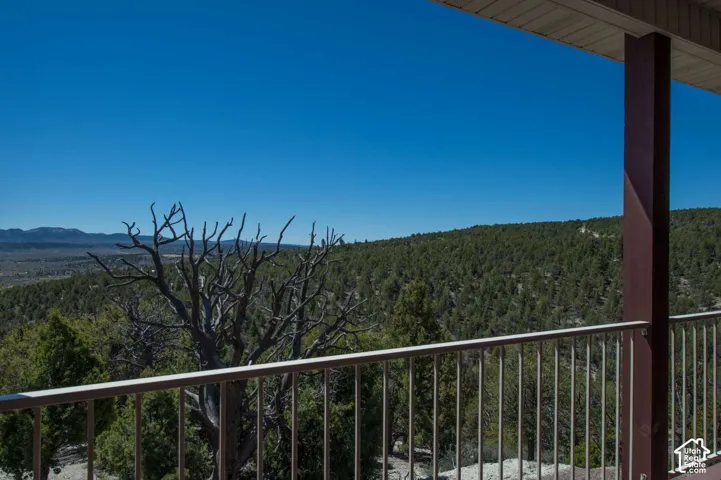 Exterior balcony with metal railing, supported by a structural column, overlooking a vast, forested landscape and distant mountains