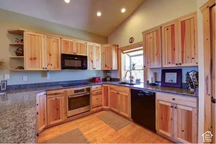 Vaulted ceiling with recessed lighting, wood-finish flooring, wood cabinetry with exposed grain, built-in stainless steel oven, and an undermount sink