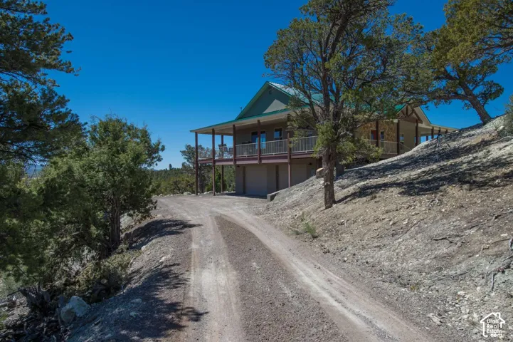 Sloped terrain with a gravel driveway, multi-level dwelling with a covered porch, and a second-story balcony