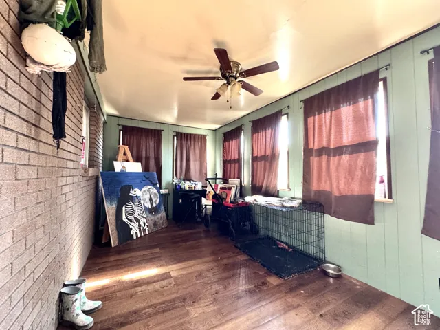 Enclosed porch featuring wood-finish flooring, brick wall, multiple windows, and a ceiling fan