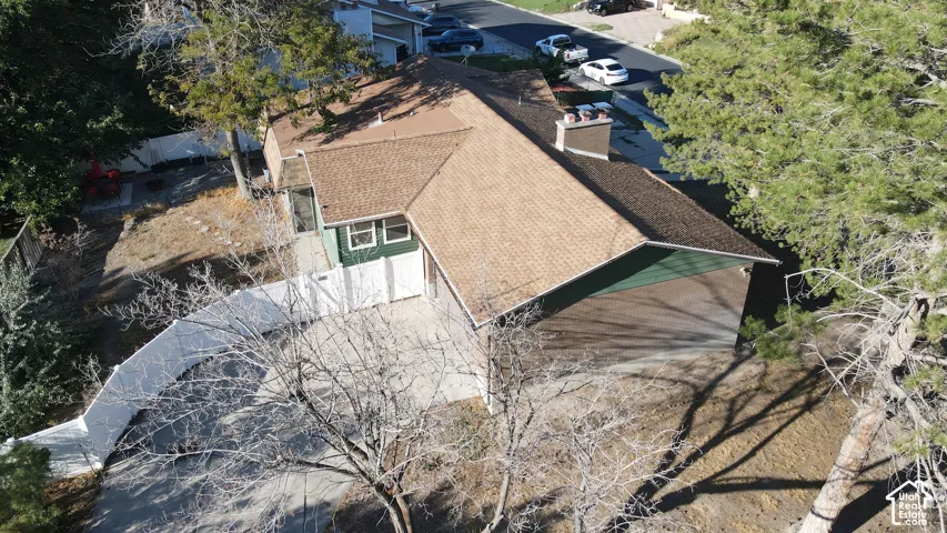 Brown shingle roof with a stone chimney, dark green exterior siding, and white garage doors