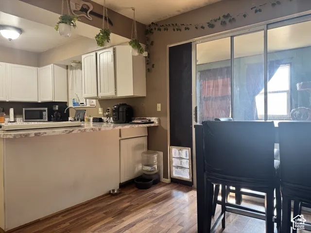 White upper and lower cabinetry, wood-finish flooring, L-shaped countertop, recessed lighting, and sliding glass panel doors