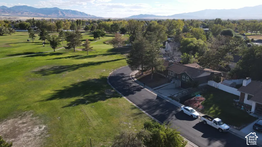 Expansive green space with mature trees, paved pathway, mountain backdrop, and surrounding residential properties