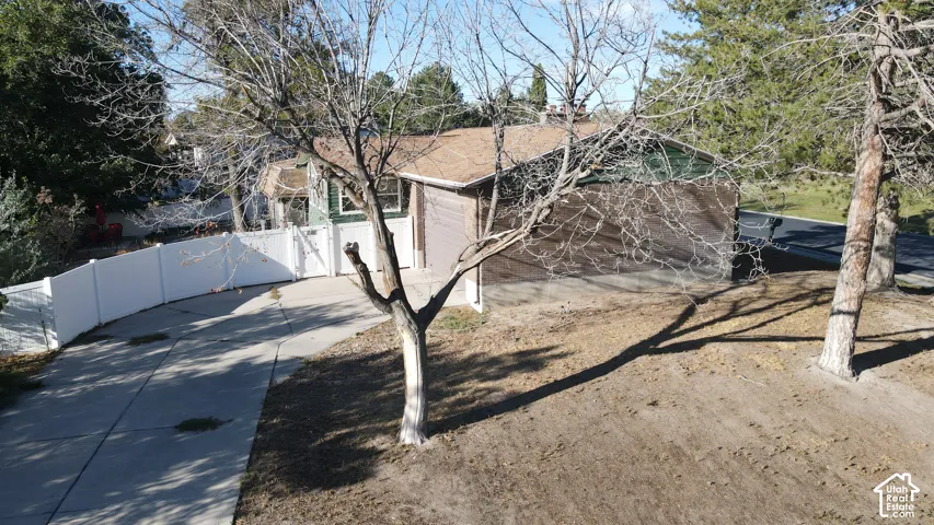 Gable roofline, attached garage, concrete driveway, white privacy fencing, and mature trees