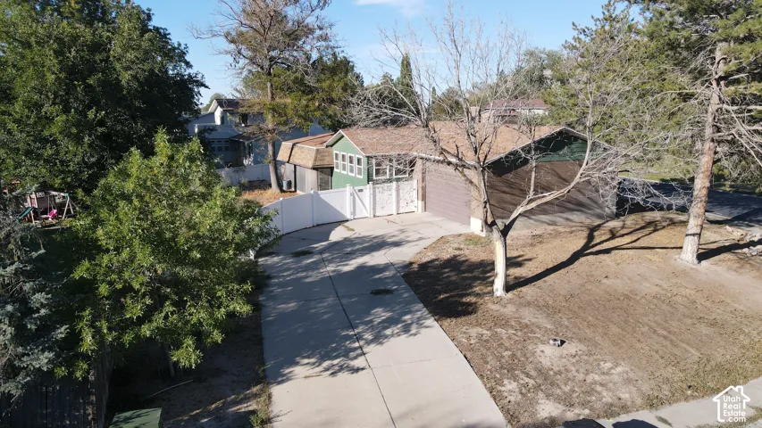 Concrete driveway, attached garage, white privacy fence, mature trees, and shingle roofing