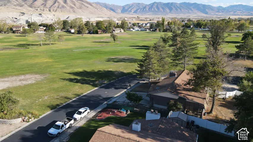 Green expanse of golf course, distant mountainous terrain, residential structures, paved roadway, mature trees