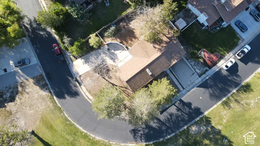 Residential property featuring a shingled roof, paved driveway, and mature trees
