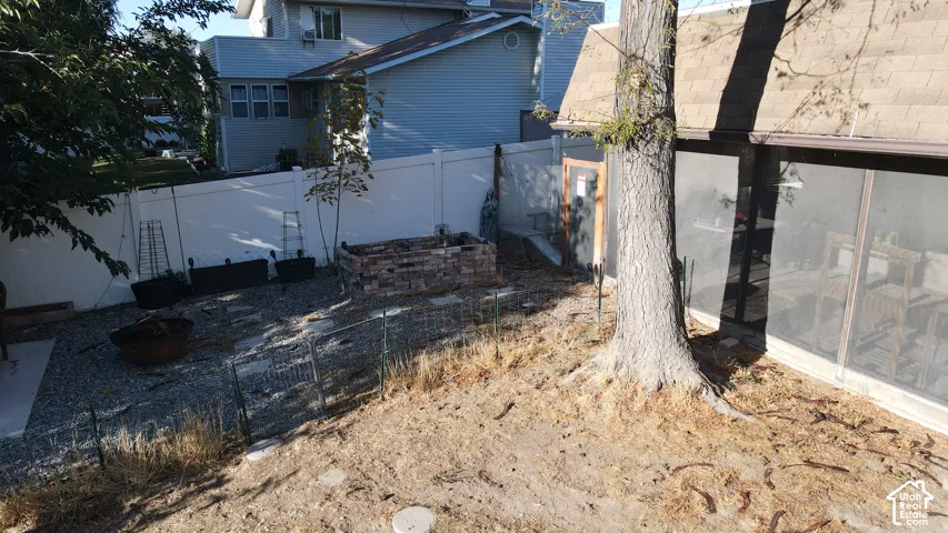 Enclosed backyard featuring a gravel patio area, brick planter box, and a white privacy fence