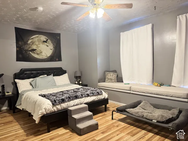 Wood-finish flooring, ceiling fan with integrated lighting, window seating, and a tufted headboard